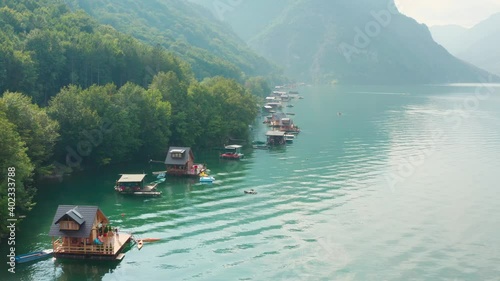 Aerial, Wooden houses floating on Perucac lake surrounded by mountains on the foggy day. photo
