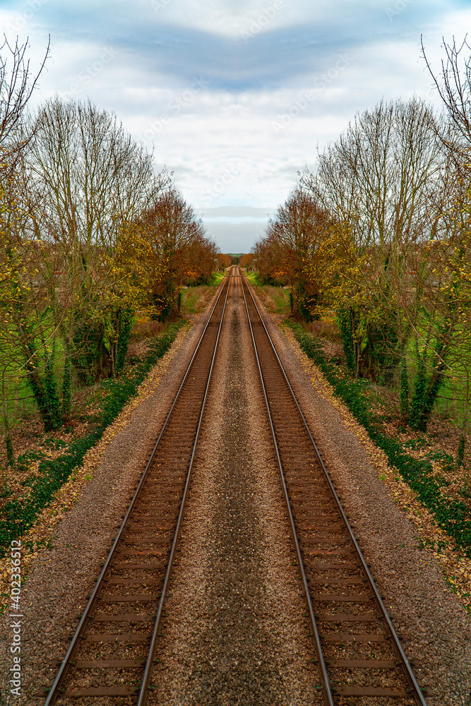 Symmetrical train tracks shot taken with view down and into the distance. Trees line both sides of the railway lines