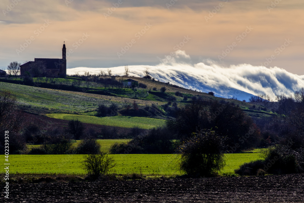 Rural landscape in the countryside with church on top of a mountain and mountains with clouds and fog.
