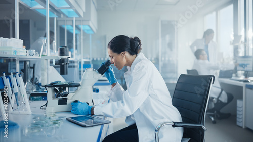 Fotografie Medical Development Laboratory: Portrait of Beautiful Caucasian Female Scientist Looking Under Microscope, Analyzes Petri Dish Sample