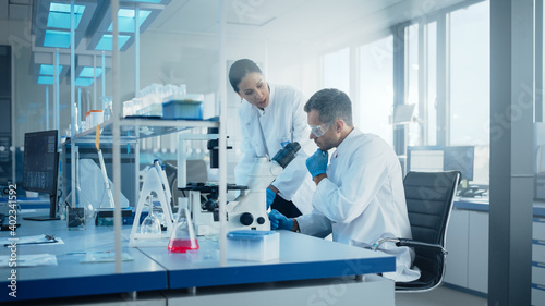 Modern Medical Research Laboratory: Portrait of Two Scientists Working, Using Microscope, Analyzing Samples, Talking. Advanced Scientific Pharmaceutical Lab for Medicine, Biotechnology Development
