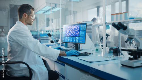 Medical Science Laboratory: Microbiologist Working on Computer with Display Showing Gene Editing Interface. Diverse Multi-Ethnic Team of Biotechnology Scientists Developing Drugs.