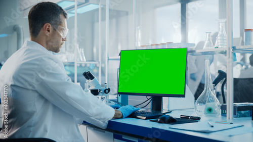 Medical Science Laboratory: Microbiologist Working on Computer with Display with Green Chroma Key Screen. Diverse Multi-Ethnic Team of Biotechnology Scientists Developing Drugs.