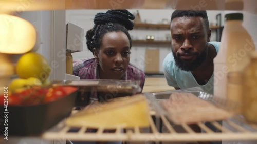 Afro-american couple opening fridge and wrinkling face having food spoiled