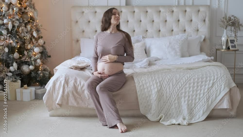 pregnant woman looking at belly while sitting on bed in christmas