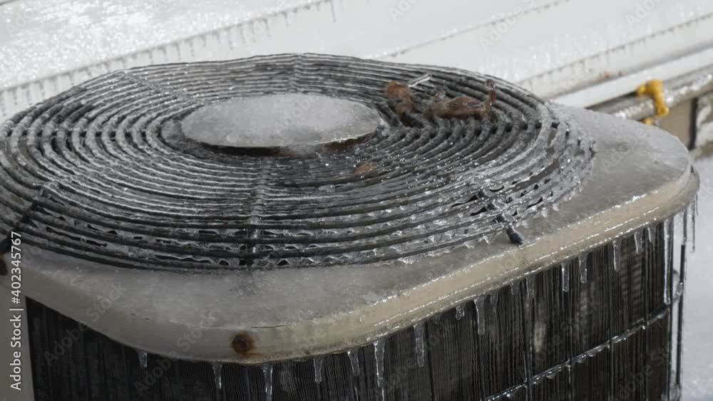 Outdoor residential A/C unit covered in ice after a winter storm.  Demonstrates need for covering outdoor appliances and equipment, changing seasons, winter ice storm effects on home exterior.