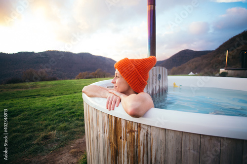 Fototapeta Happy romantic woman in big beanie hat sit inside warm big wooden hot tub