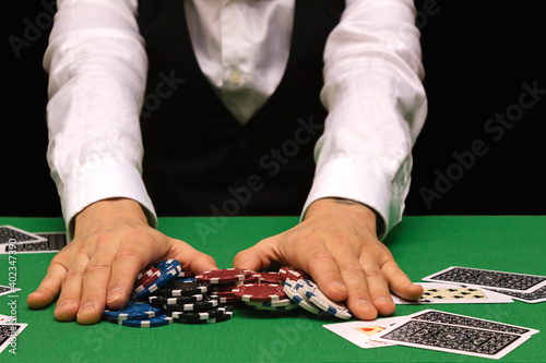 Fotografie Male professional poker player placing a bet playing the game of poker in a casino with green baize and black copy space