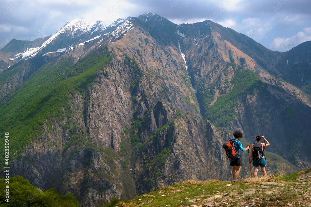 Girls hikers with backpack and trekking poles walk along a path in a panoramic point of the Val Grande National Park, Europe, Piedmont Italy.