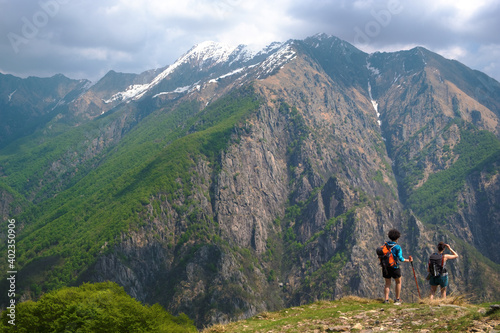 Couple of young women hiking along a mountain path, in the background the wild panorama of the Val Grande National Park, Europe, Piedmont Italy.