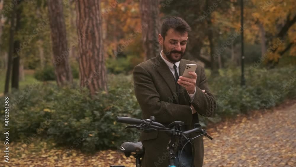 Handsome young man with electric bicycle using mobile phone in the autumn park Handsome young man with electric bicycle using mobile phone in the autumn park