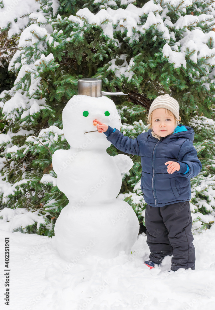 Happy child playing with a snowman outdoor in winter. Cute little child building a snowman and having fun in park or backyard. Happy child playing with a snowman outdoor in winter. Cute little child building a snowman and having fun in park or backyard.