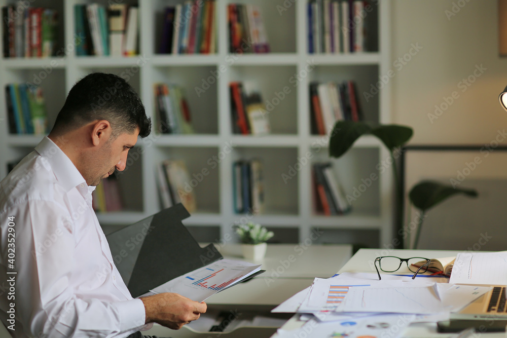 Young businessman in eyeglasses working on computer at homeoffice. Employee in eyeglasses holding paper documents, young businessman analyzing and working with documents. Young businessman in eyeglasses working on computer at homeoffice. Employee in eyeglasses holding paper documents, young businessman analyzing and working with documents.
