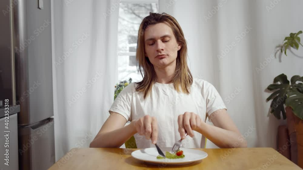 Young man sitting on chair and eating tomato and salad on plate. Young man sitting on chair and eating tomato and salad on plate.