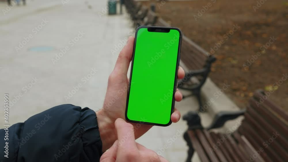 Close up hands man holding use phone with vertical green screen in park background bench. Internet finger gadget device. Slow motion