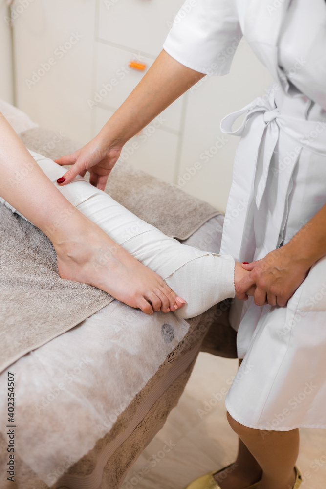 The massage therapist in the spa beauty salon makes a wrap to the client to get the body in shape, get rid of puffiness