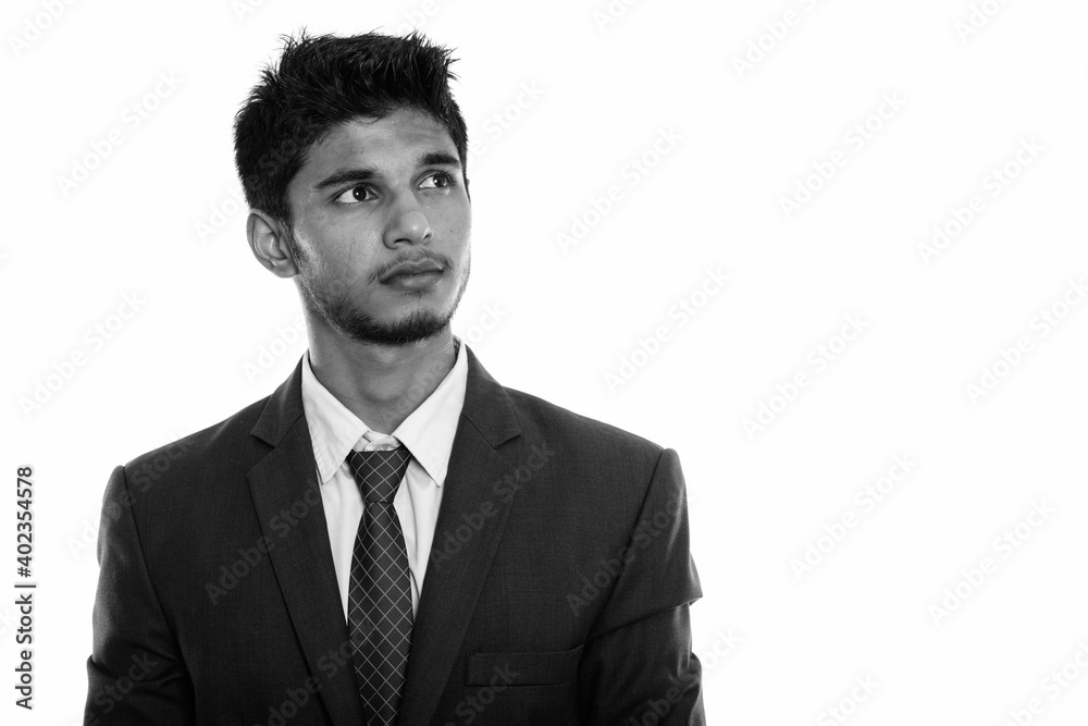 Studio shot of young handsome Indian businessman thinking while looking up Studio shot of young handsome Indian businessman thinking while looking up