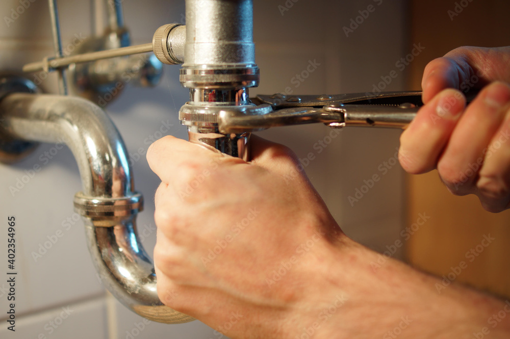 Obraz premium Young plumber is fixing a pipe with a wrench in the bath.