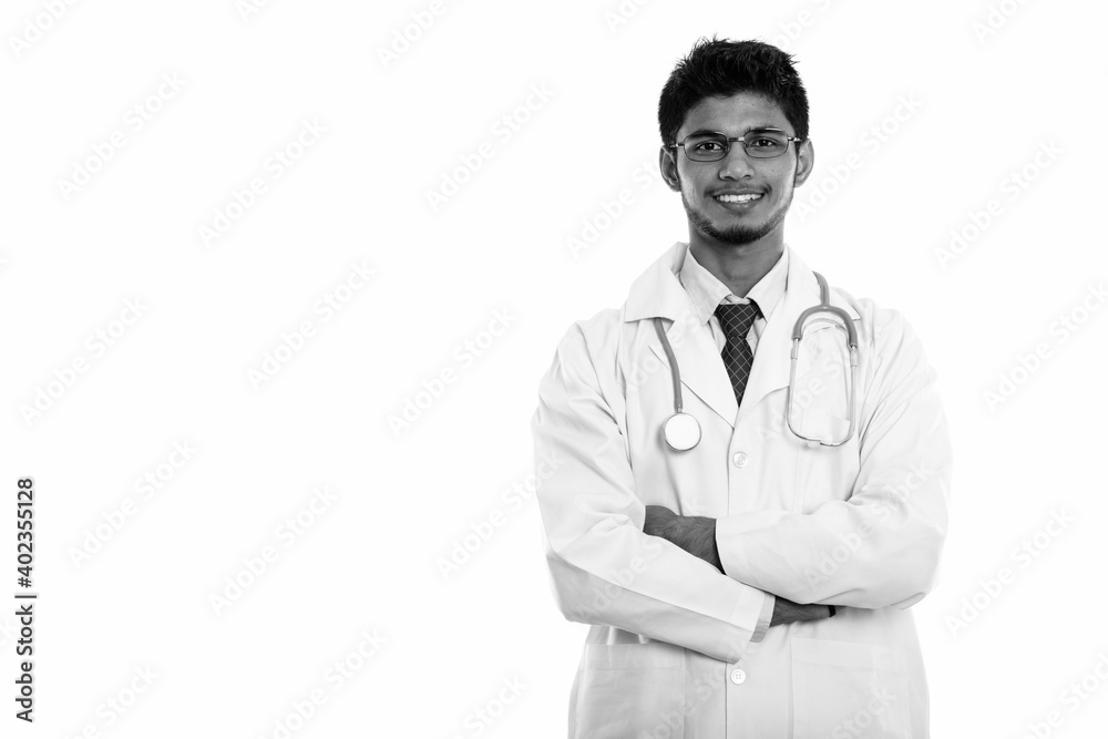 Studio shot of young happy Indian man doctor smiling with arms crossed Studio shot of young happy Indian man doctor smiling with arms crossed