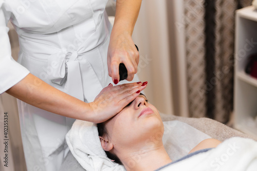 Woman client in salon receiving manual facial massage from beautician
