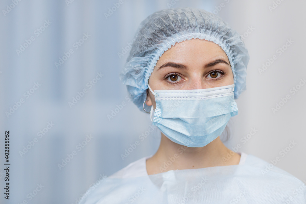 Close-up portrait a young female doctor in a protective medical mask and hat. Hispanic woman looking at the camera on a white background in a hospital room. Portrait of ambulance nurse Close-up portrait a young female doctor in a protective medical mask and hat. Hispanic woman looking at the camera on a white background in a hospital room. Portrait of ambulance nurse