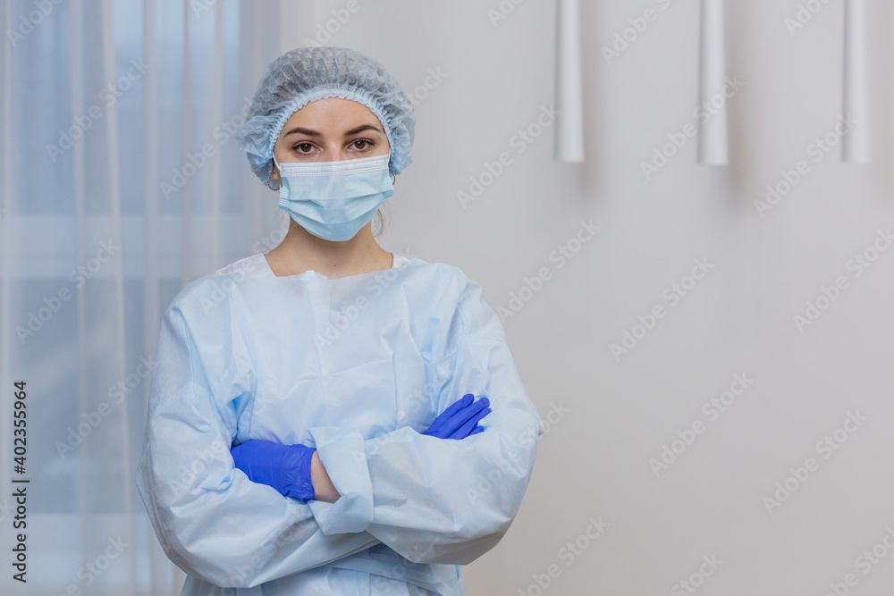Close-up portrait a young female doctor in a protective medical mask and hat. Hispanic woman looking at the camera on a  white background in a hospital room. Portrait of  ambulance nurse