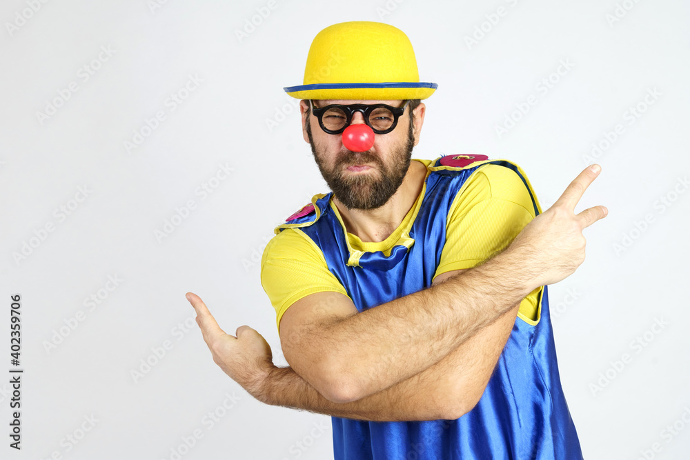 A clown in a bright blue and yellow suit hugs himself and shows hand gestures