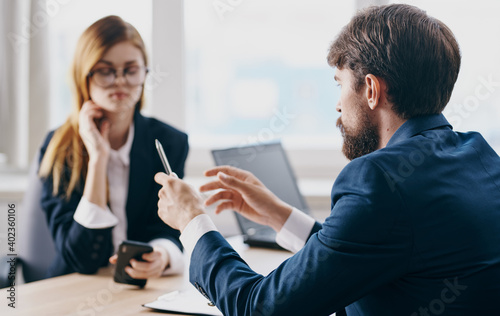 A business man in a suit and a woman communicate at work opposite each other at the table in the office