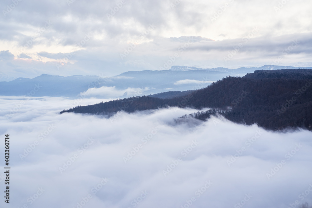 Low clouds, view of winter forest and mountains from observation deck, horizontal picture of amazing natural phenomenon. Beautiful unreal panoramic view of mountains in clouds. Low clouds, view of winter forest and mountains from observation deck, horizontal picture of amazing natural phenomenon. Beautiful unreal panoramic view of mountains in clouds.