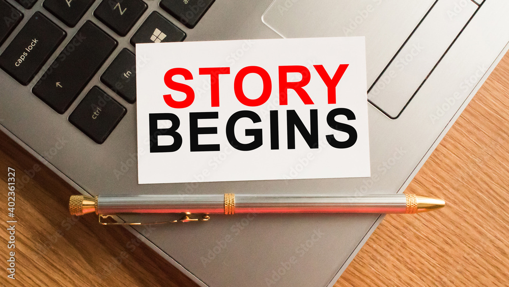 Notepad with the text STORY BEGINS is on the laptop keyboard. Minimal work space. Business concept.