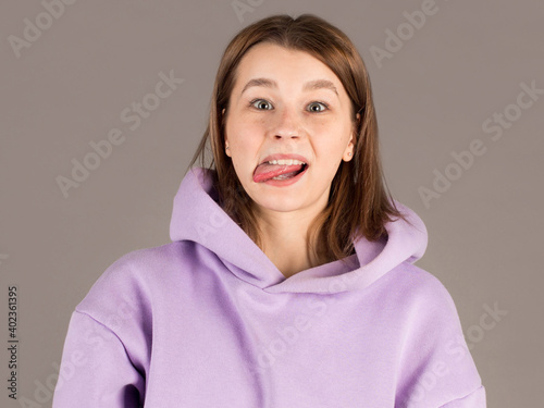 Bilde på lerret Funny cute young woman smiling showing tongue looking at camera over gray background