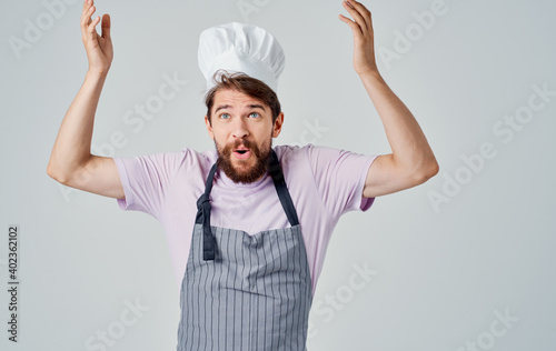 A cook in a headdress is gesturing with his hands on a light background, success emotions