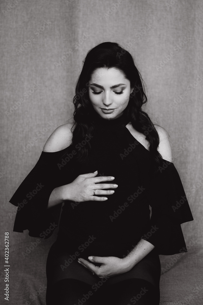 Fototapeta premium Pregnancy photo session in a photo studio with a fabric background in a black bodysuit and tights 