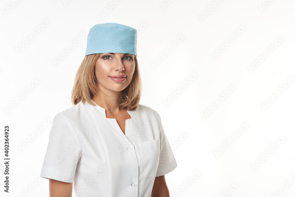 Isolated portrait of a young cute doctor wearing white uniform and blue medical hat standing on white background and smiling at camera Isolated portrait of a young cute doctor wearing white uniform and blue medical hat standing on white background and smiling at camera