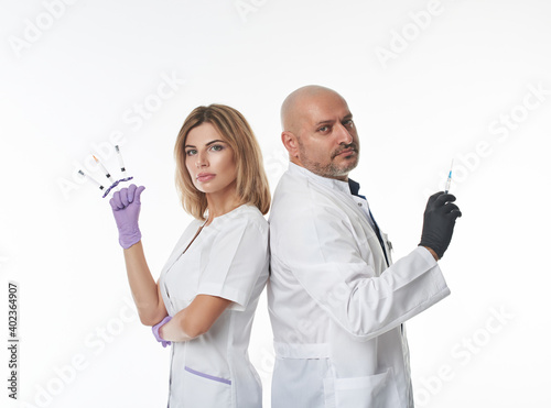 Isolated portrait on a white background of two doctors (male and female) standing with their backs to each other and holding syringes between fingers. Team. photo