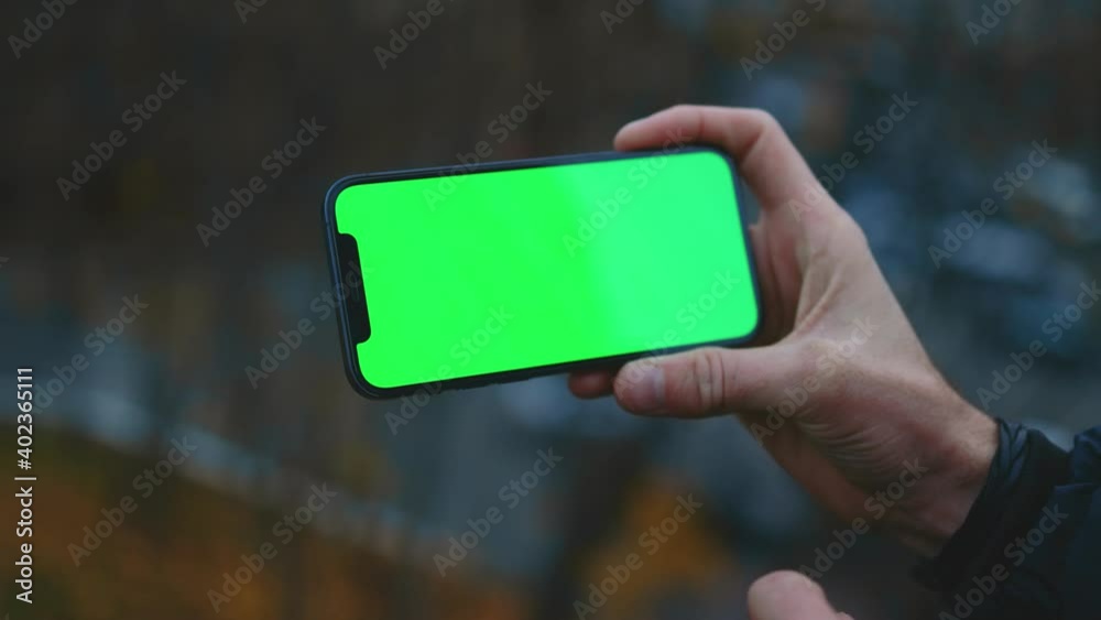 Shot of man hand using and tapping phone with horizontal green screen on blurred background view in old town blurred. Touchscreen message cellphone. Slow motion Shot of man hand using and tapping phone with horizontal green screen on blurred background view in old town blurred. Touchscreen message cellphone. Slow motion