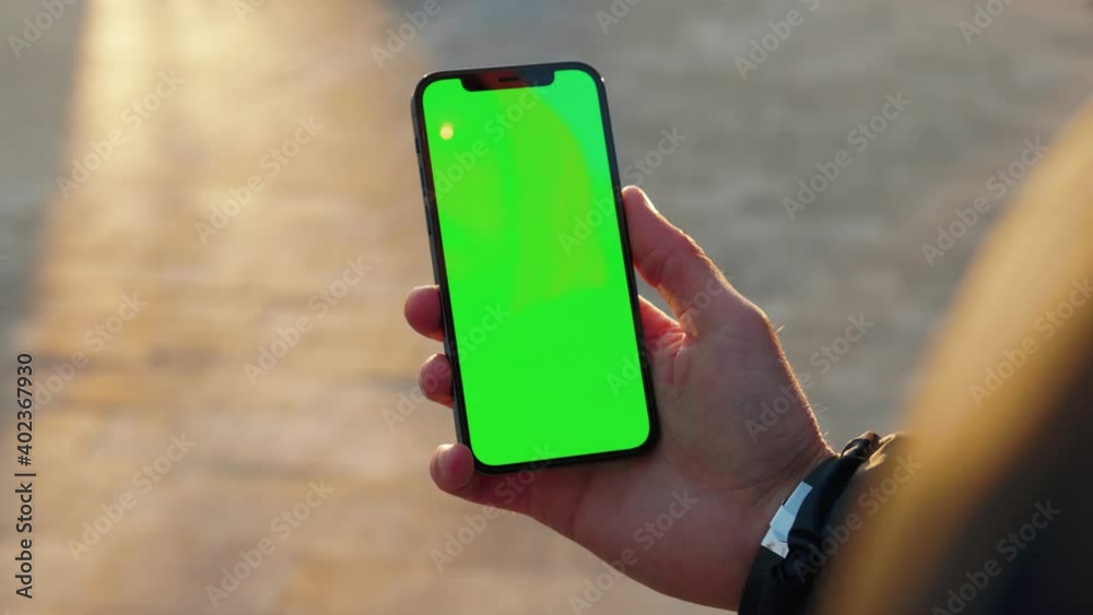 Close up man young hand using touch phone with vertical green screen background sunlight road in city blurred. Internet chrome outdoor cellular smartphone scrolling tapping. Slow motion