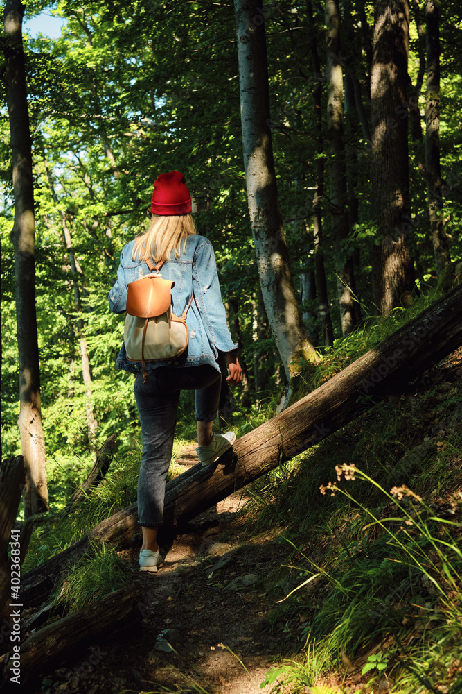 A woman traveler walks through the forest. Beautiful nature landscape in woods. Hiking journey on tourist trail. Outdoor adventure. Travel and exploration. Healthy lifestyle, leisure activities A woman traveler walks through the forest. Beautiful nature landscape in woods. Hiking journey on tourist trail. Outdoor adventure. Travel and exploration. Healthy lifestyle, leisure activities