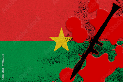 Burkina Faso flag and black RPG-7 rocket-propelled grenade launcher in red blood. Concept for terror attack or military operations with lethal outcome photo