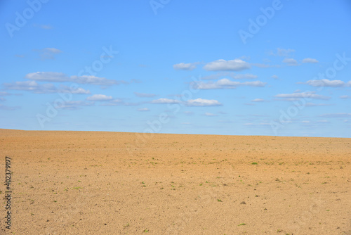 View of a deserted sand field against a blue sky with clouds.