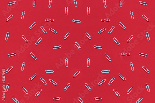 White paper clips are scattered on a red background. Top view, flat lay. Back to school, college, education concept. Abstract background