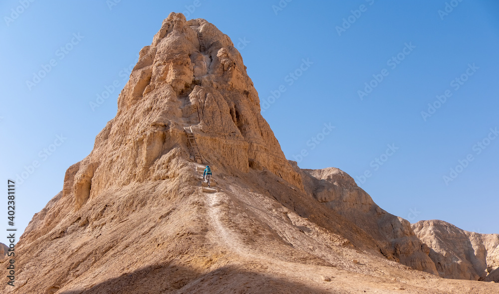 Young female hiker going along a steep mountain ridge. Hard and dangerous hiking trail in Judean Desert. Extreme climbing and adrenaline. Ropes and wood ladders on a trail.