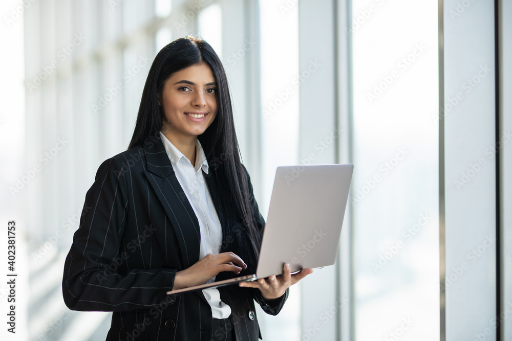 Young business woman with laptop standing in an office windows Young business woman with laptop standing in an office windows