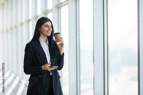 Young business woman use phone for text or surfing in internet with coffee cup in hands in modern office.