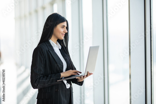 Young business woman with laptop standing in an office windows