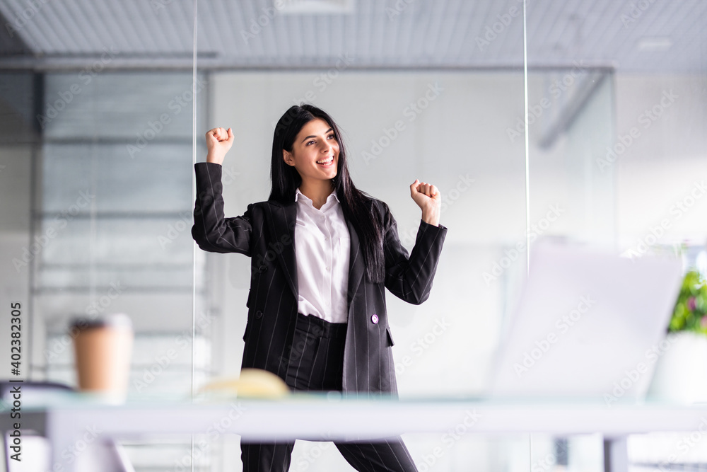 Excited young businesswoman celebrating success looking above at office