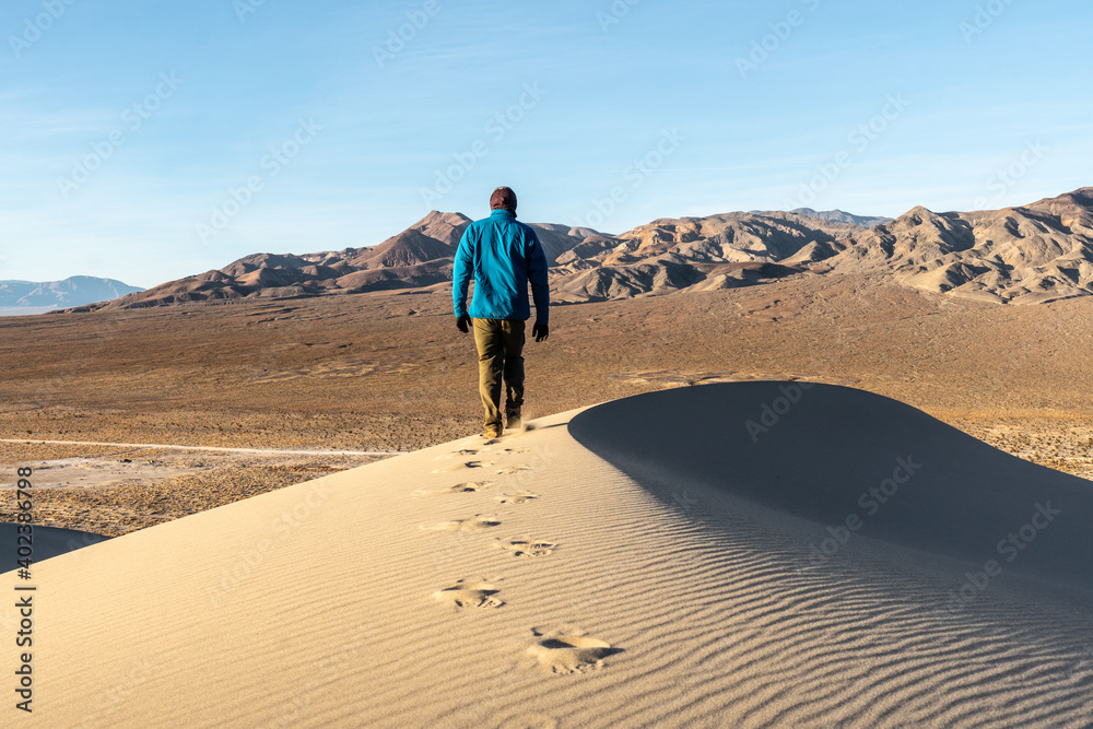 A hiker person man hiking on a sand dune leaving a track as he goes with a ridgeline clearly visible, no wind, Eureka Dunes, Death Valley National Park, California