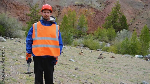 Portrait of a mining engineer, a geologist in the protective reflective vest, gloves and helmet, with hammer in hand.