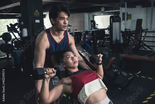 A young asian man spotting an athletic girl doing incline dumbbell presses. Working out with assistance at the gym. photo