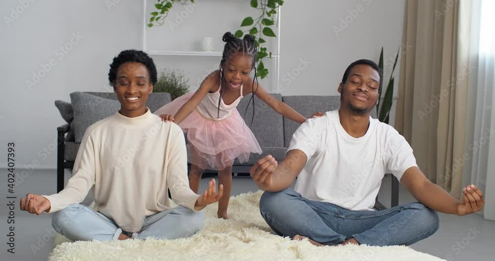 Young couple afro american woman moms and black man dad sit in lotus position do yoga breathing exercises for calm get rid of stress, little girl board naughty child noises pushing parents interferes Young couple afro american woman moms and black man dad sit in lotus position do yoga breathing exercises for calm get rid of stress, little girl board naughty child noises pushing parents interferes